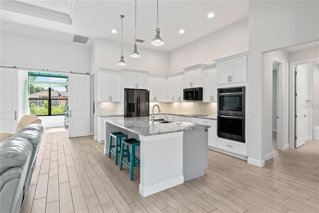 Kitchen featuring black appliances, white cabinets, decorative backsplash, light stone countertops, and a kitchen island with sink