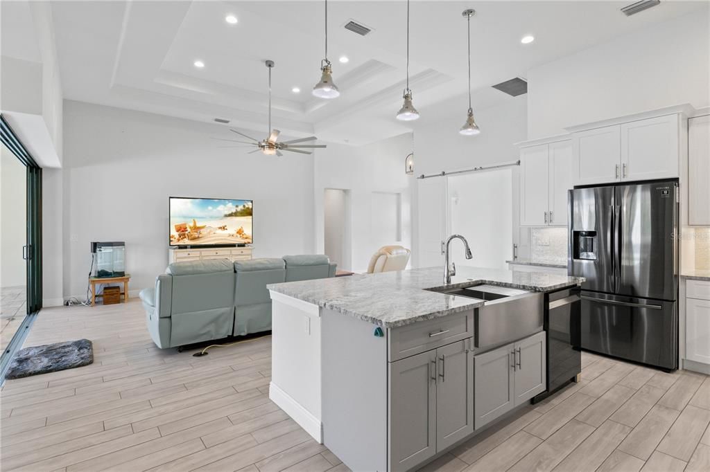 Kitchen featuring an island with sink, ceiling fan, a towering ceiling, decorative backsplash, and stainless steel fridge