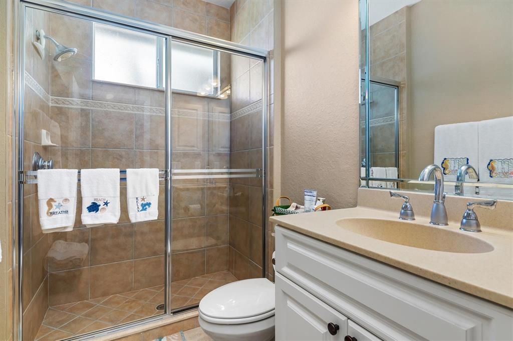 Guest bathroom with glass slider to walk-in tile shower, bright and airy with window, situated in hallway between bedroom 2 and 3, cultured granite vanity, under kick board lighting for ease at night.