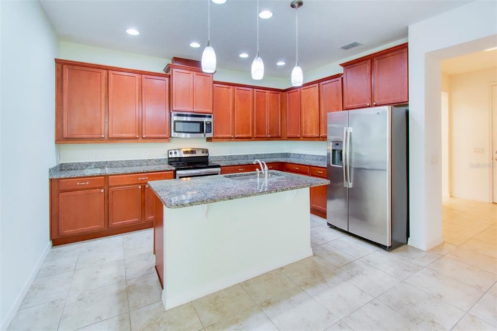 Ample WOOD cabinets - finished in a pecan stain, with GRANITE counters, and pendants at the LARGE ISLAND too!