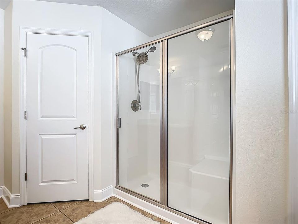 Bathroom with big shower with double shower heads, enclosed toilet and linen closet