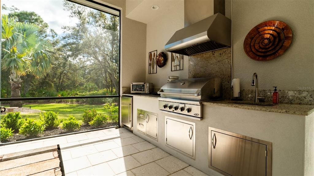 Outdoor kitchen includes a grill, hood vent, sink and refrigerator.