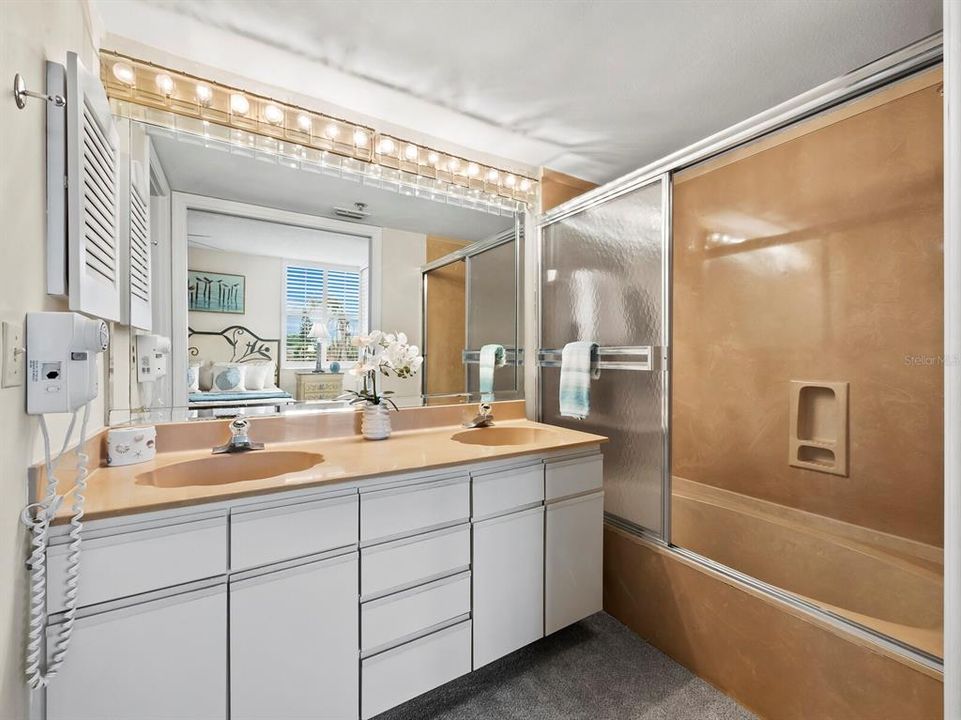 The primary bedroom's en-suite bathroom features a dual sink vanity, Hollywood lighting, plenty of vanity storage, and an enclosed bathtub/shower combination.