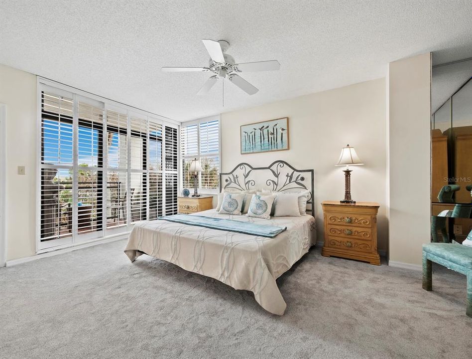 The expansive Primary Bedroom boasts high ceilings, sliding glass doors that lead to a private balcony, and plantation shutters.