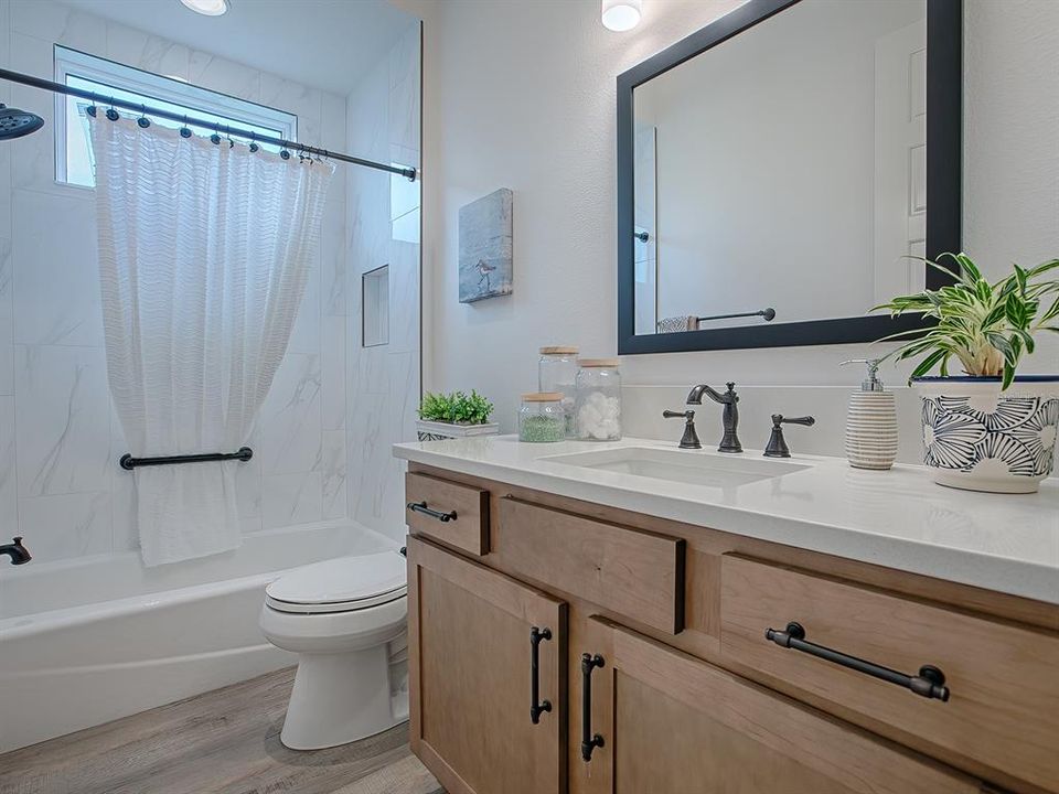 GUEST BATH WITH TUB/SHOWER, QUARTZ COUNTERTOPS AND FRAMED MIRROR.