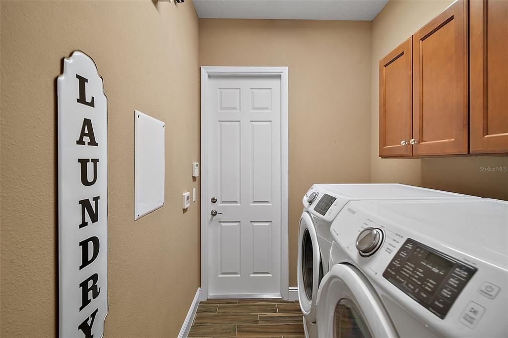 The laundry room sits just off the kitchen with a Samsung front-load washer and dryer. It also includes a sink and extra storage above appliances. Doorway to 2-car garage