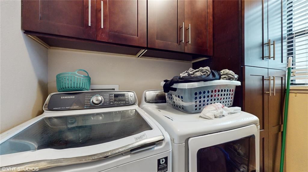 Samsung washer and dryer with cabinets for storage and shelf for hanging clothes in laundry room.