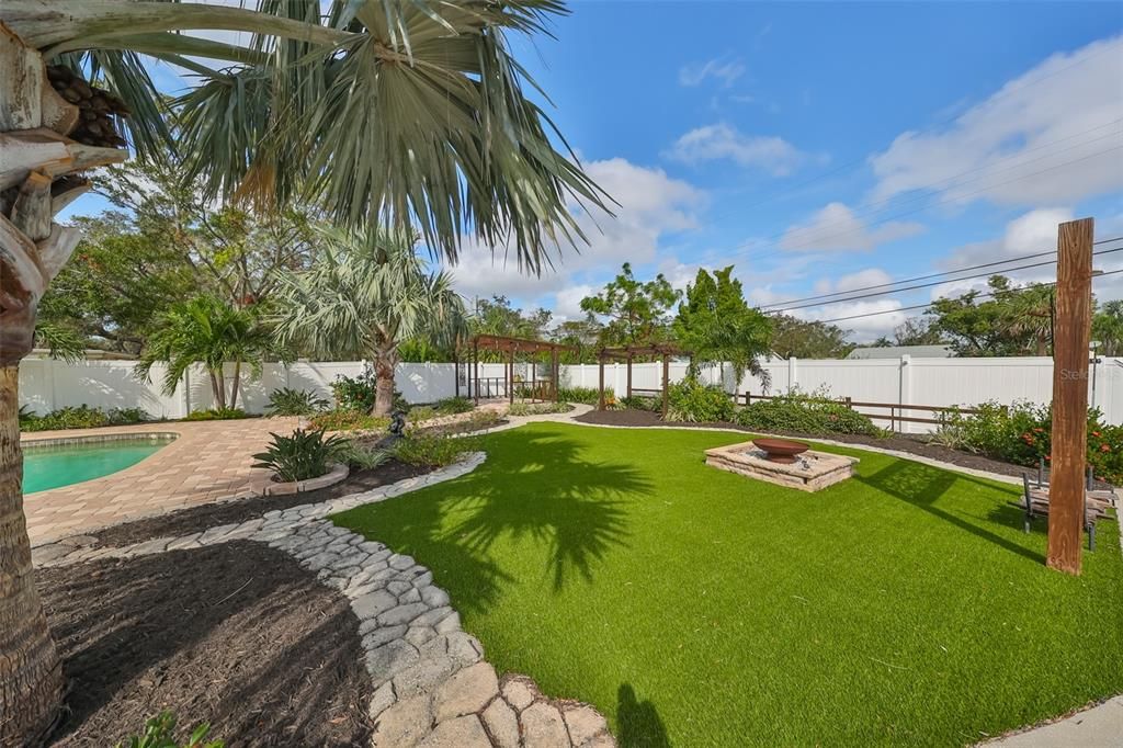 View of the resort style backyard with mature landscaping and low maintenance artificial turf