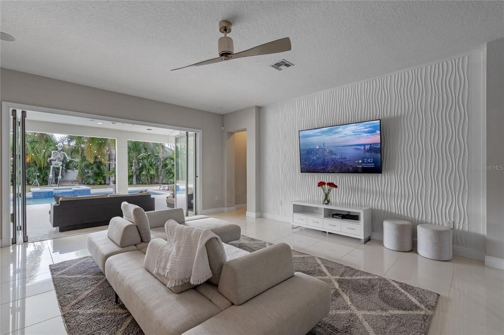 The living room features bi fold sliding doors that open onto the covered lanai and outdoor  kitchen