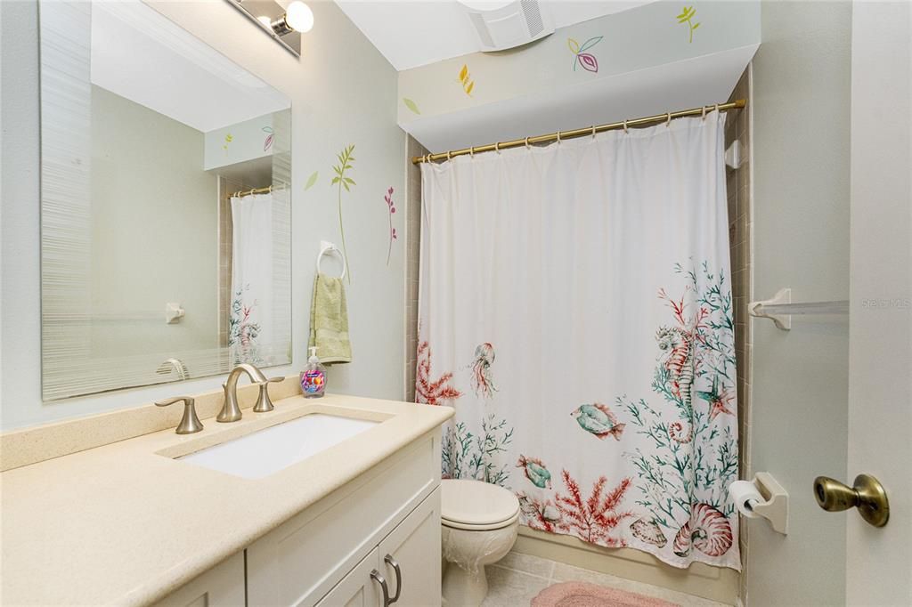 The guest bathroom has an updated vanity with a solid surface counter top and tiled flooring.