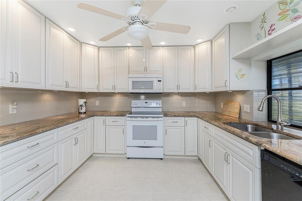 The kitchen has updated cabinetry with granite countertops, a tiled backsplash and a ceiling fan.