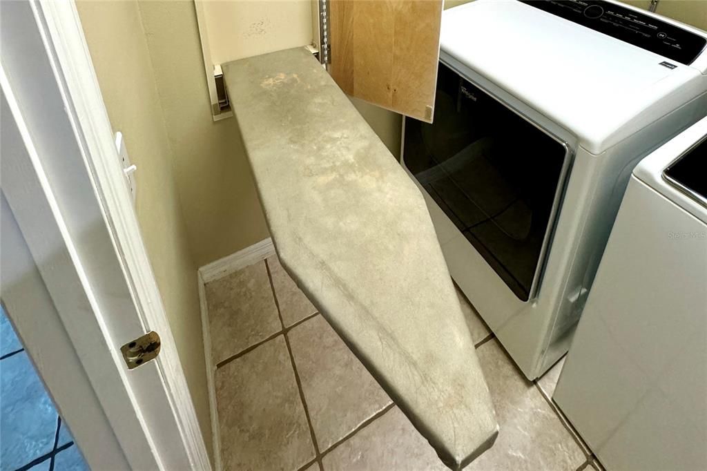 This well-appointed laundry room offers convenience and functionality with an included Whirlpool washer and dryer, easy-maintenance tile flooring, a storage shelf above the appliances, and a built-in fold-down ironing board wired for an iron. Designed to streamline daily routines, this utility space is both stylish and efficient.