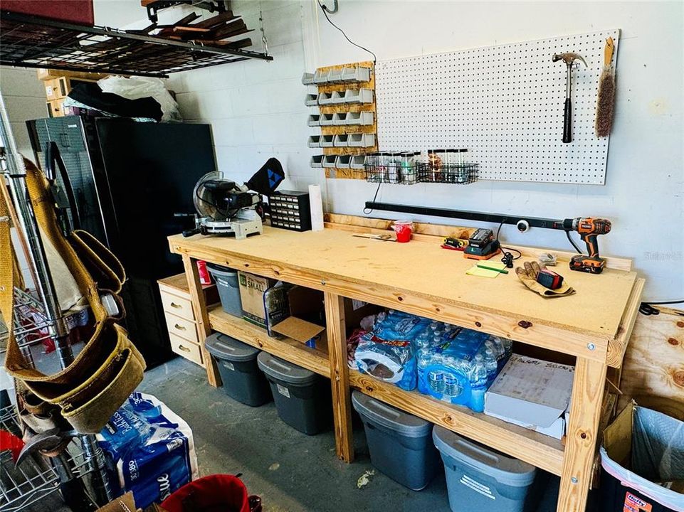 This functional side-facing two-car garage is ideal for storage and projects, equipped with a Carrier HVAC system with UV light kit, water heater, and a spare refrigerator that will stay. A custom-built workbench with drawers, shelving, and a pegboard provides a perfect DIY setup, with additional overhead storage racks for organization. The garage includes a Wayne Dalton automatic door opener with safety reversal and one remote, along with pre-cut, labeled wood for window coverage during hurricanes. This versatile space is ready to support hobbies, home maintenance, and extra storage needs.