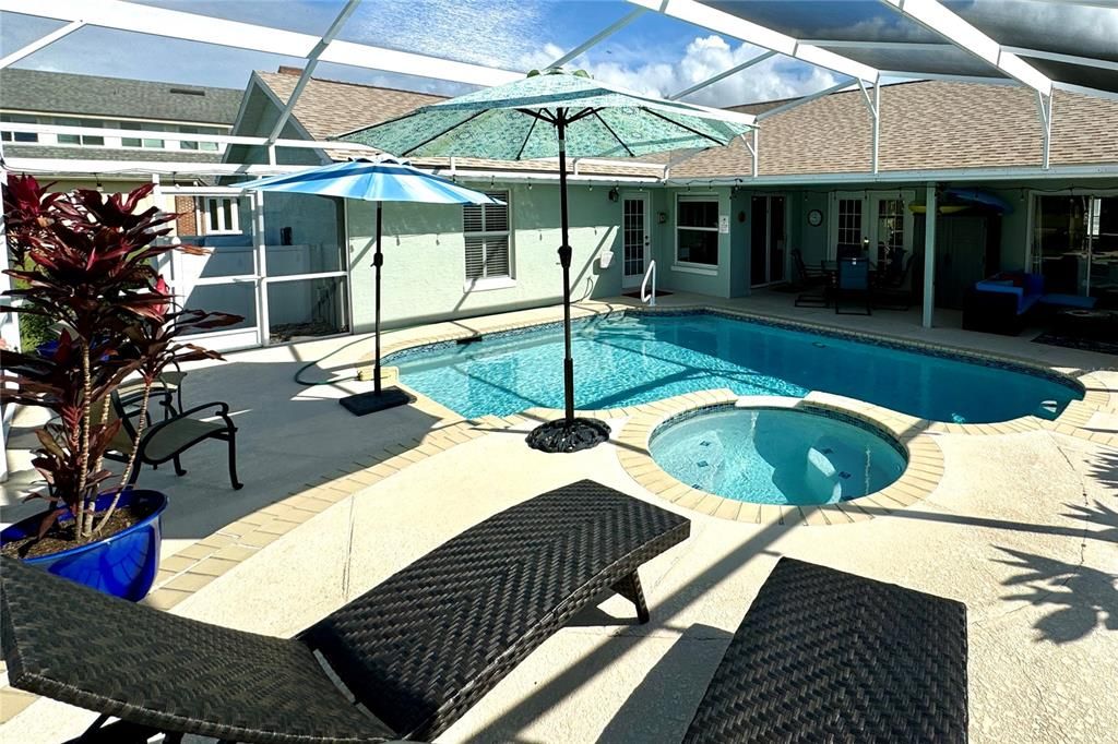 This beautiful screened-in pool area offers a resort-like setting with a sparkling pool and an elevated spillover spa, perfect for relaxation and entertainment. The pool’s design features a spacious deck with ample room for lounging and dining, while the raised spa cascades into the pool, creating a soothing waterfall effect. Beyond the pool, enjoy a tranquil view of the nearby pond, providing a peaceful backdrop to this outdoor oasis. The surrounding landscaping and privacy screens add an extra layer of seclusion. In the evenings, string lights around the enclosure create a warm and inviting ambiance, transforming the space into a serene retreat under the stars. This outdoor area is ideal for both daytime enjoyment and evening relaxation, combining elegance with a touch of nature.