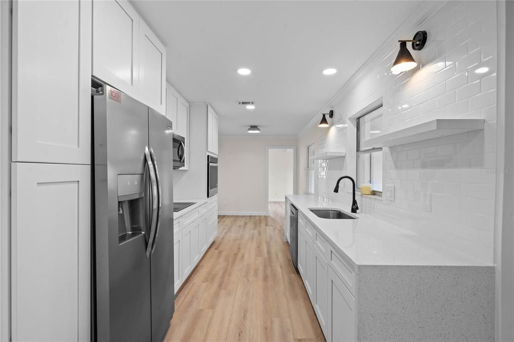 Gorgeous kitchen complete with counter to ceiling subway tile, floating shelves, waterfall edge quartz counters and wall lighting