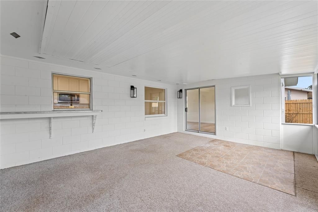 Large back porch with passthrough to to kitchen and sliding doors leading into the primary bedroom