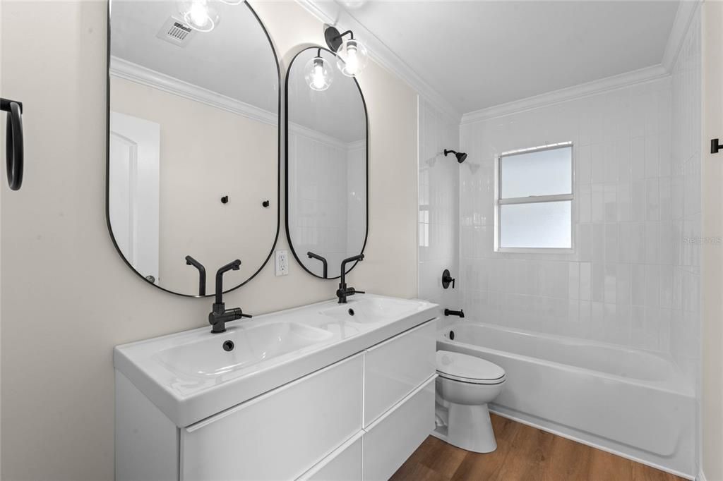 Secondary bathroom features double sink vanity, tub with shower and gorgeous mirrors and lighting