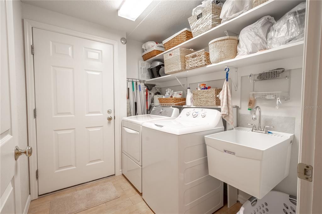 The laundry room features ceramic tile flooring, overhead shelving, washer and dryer hook-ups, and a utility sink.