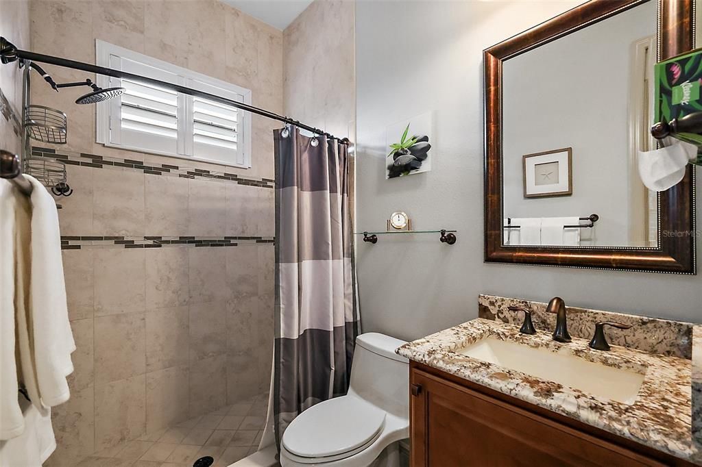 The guest bath is ensuite to the office/den with a low-step shower with ceramic tile and inlay.