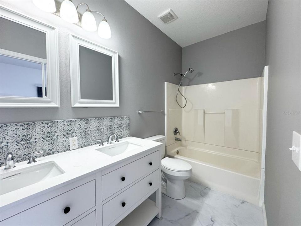 Primary ensuite with new vanity, lighting, mirrors, backsplash, flooring, and exhaust fan