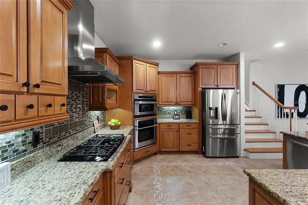 KITCHEN - The spacious kitchen features stainless steel appliances including gas cooktop, exhaust hood, convection oven, microwave/combination oven, breakfast bar, built-in desk, solid wood cabinetry, granite countertops, wine rack and beautiful glass/tile backsplash!...