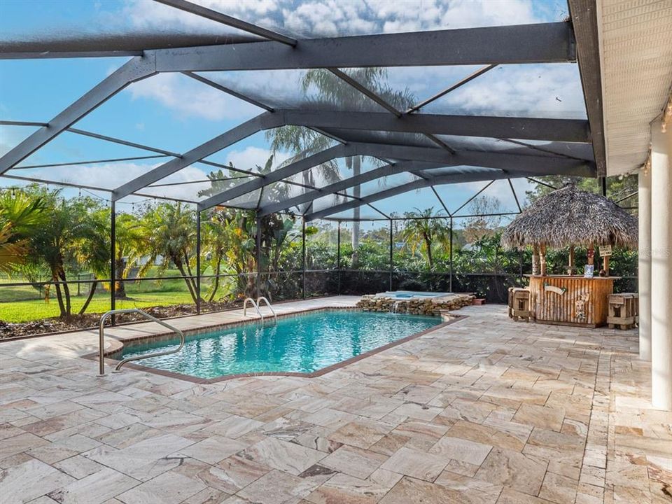 Stunning pool and spa with a spill over waterfall and a thatched Tiki bar surrounded by travertine stone tile.