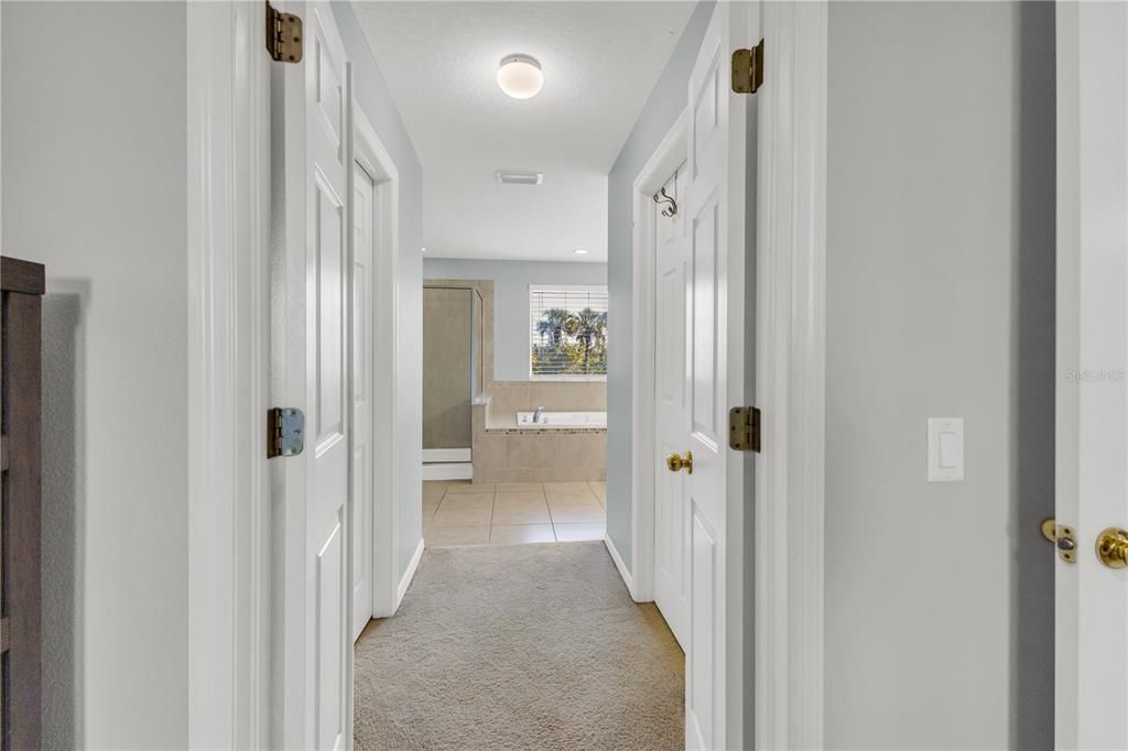 Hall from primary bedroom to the ensuite bathroom with his and hers closets on each side