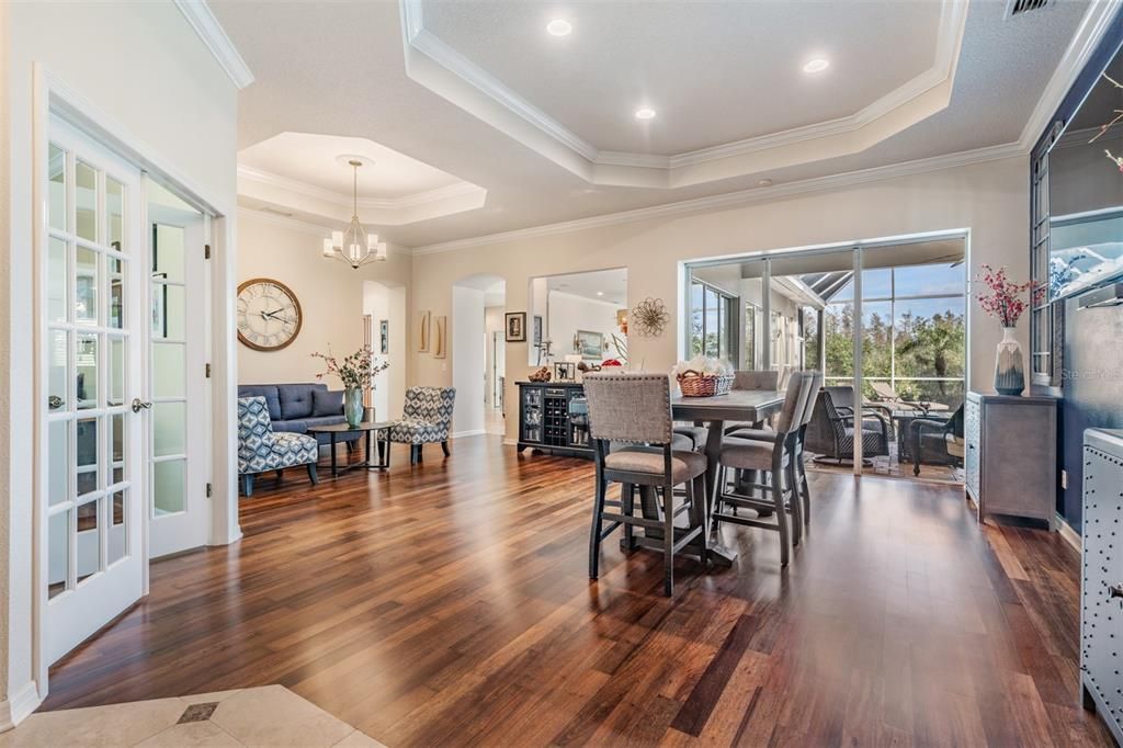 Open Dining Room with Burma Walnut Flooring, Inset Ceiling with Crown Molding, Office is on the left with the French Doors.