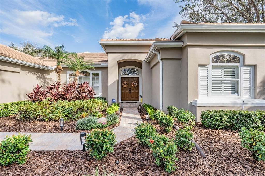 Front exterior with beautiful landscaping, Plantation Shutters, Double Front Doors and Gutters, Pool with Solar Panels, Outdoor Lighting.