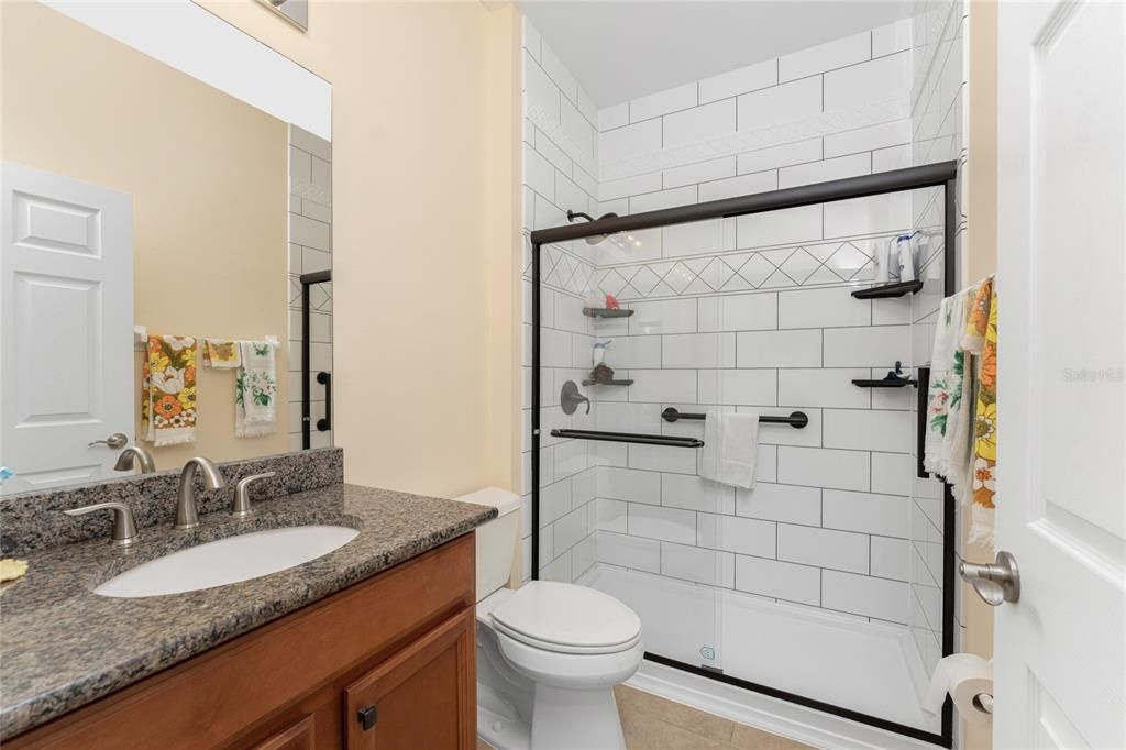 The guest bath has tiled flooring, wood vanity with granite countertop, a high rise toilet and an updated step in shower.