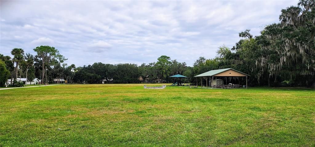 Open field with a playground, fire pit, and pavillion.