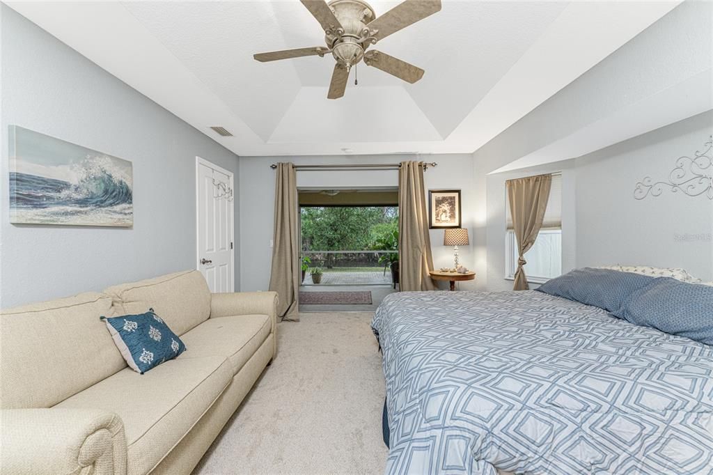 Main bedroom has a tray ceiling with a fan, updated carpeted flooring and sliding glass doors to the lanai.