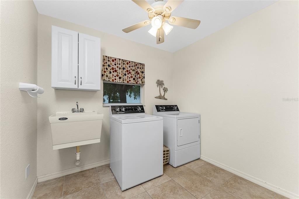 Large utility room houses a Speed Queen washer and dryer, ceiling fan and utility sink.