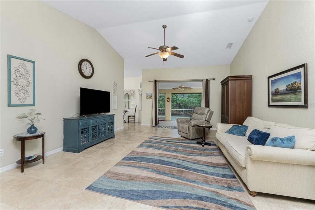 Living room features tiled flooring, cathedral ceiling with ceiling fan and sliding glass doors to the lanai.