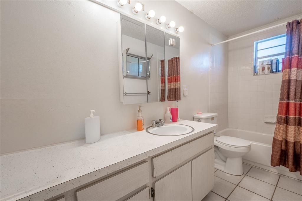 UNIT A: Bathroom features a ceramic tile floor, a mirrored vanity with storage and light fixture and a tiled tub with shower.