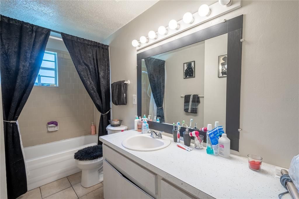 UNIT B: Bathroom features a ceramic tile floor, a mirrored vanity with storage and light fixture and a tiled tub with shower.