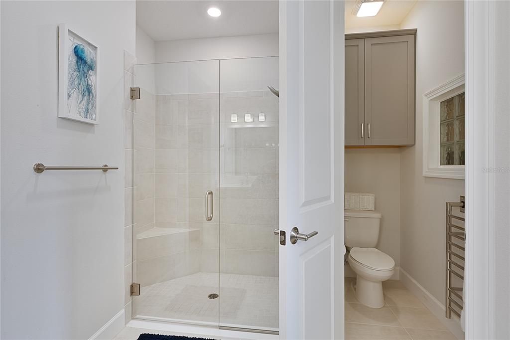 Water closet with additional cabinet and electric hardwired towel warmer.