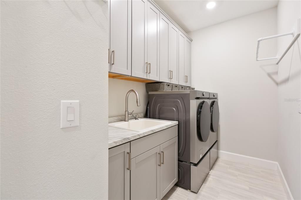 Laundry room with a deep oversized sink, plenty of cabinets, high end washer dryer with pedistals & a built in ironing board