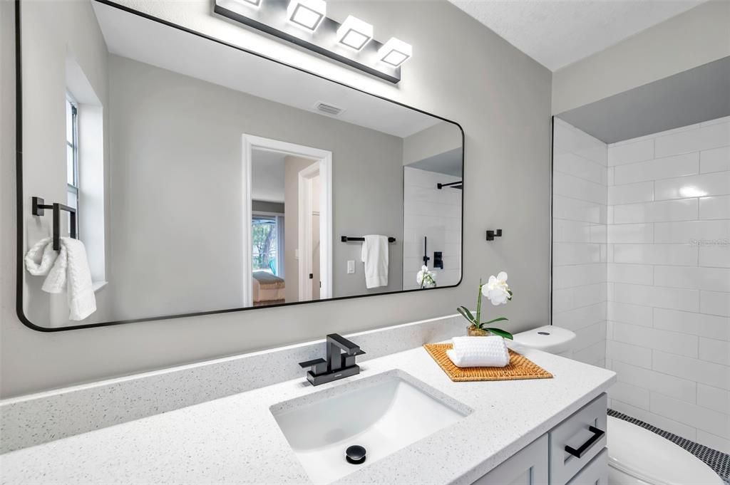 Bathroom showcasing a sleek sink with quartz countertops, a new mirror, updated lighting, and modern black accents for a sophisticated look.