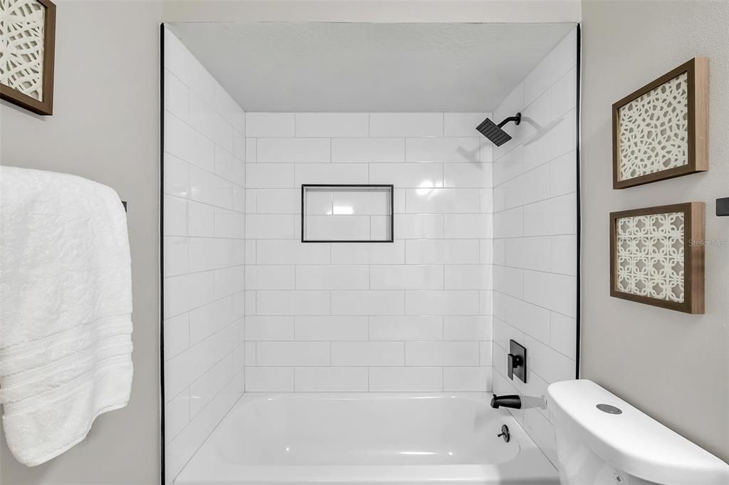 Newly remodeled guest bathroom showcasing a modern tub/shower combo with fresh tile and fixtures, paired with soft-close real wood gray shaker cabinets for a stylish touch.