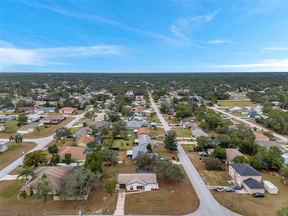 Expansive aerial views of the property, featuring mature shade trees that provide privacy and natural beauty while framing the home, spacious yard, and screened pool enclosure.