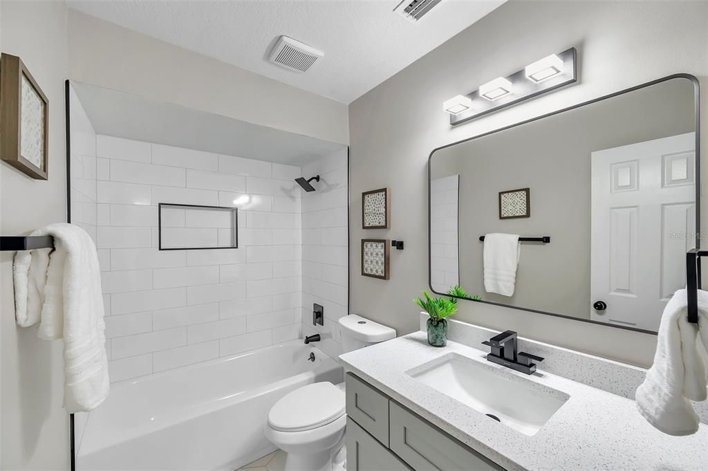 Newly remodeled guest bathroom featuring a sleek vanity with quartz countertops, soft-close real wood gray shaker cabinets, a modern mirror, and updated lighting—perfect for guests