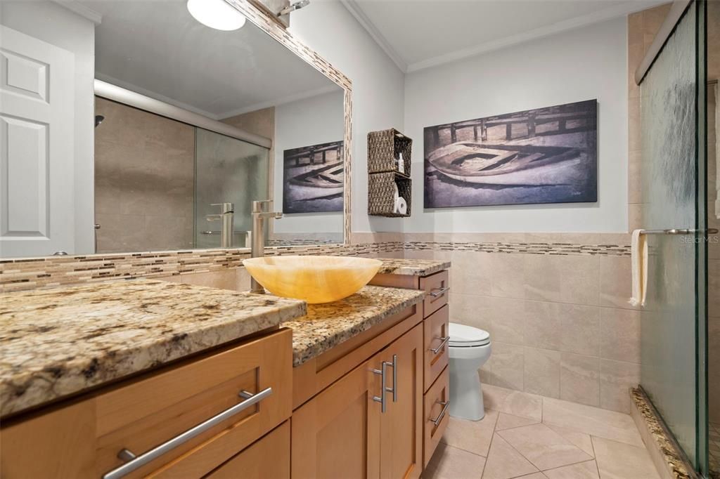 Updated with a step-in shower, a large vanity featuring stone counters and a vessel sink.