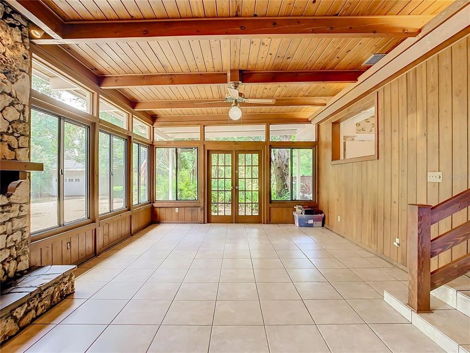 Large family room with tongue and groove ceilings with beams, wood burning fire place,  tile flooring, and French doors.