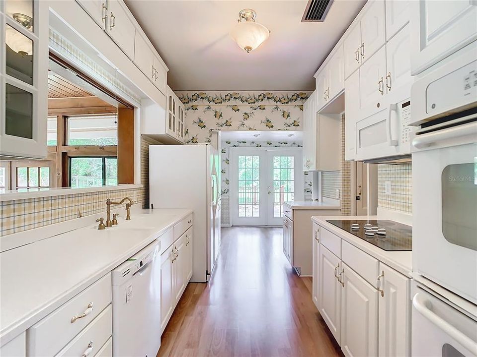 Kitchen with wood cabinetry with ample storage space, convection oven, built-in cook top, dishwasher, refrigerator, dinette area, and French doors leading to the exterior deck that faces the lake.