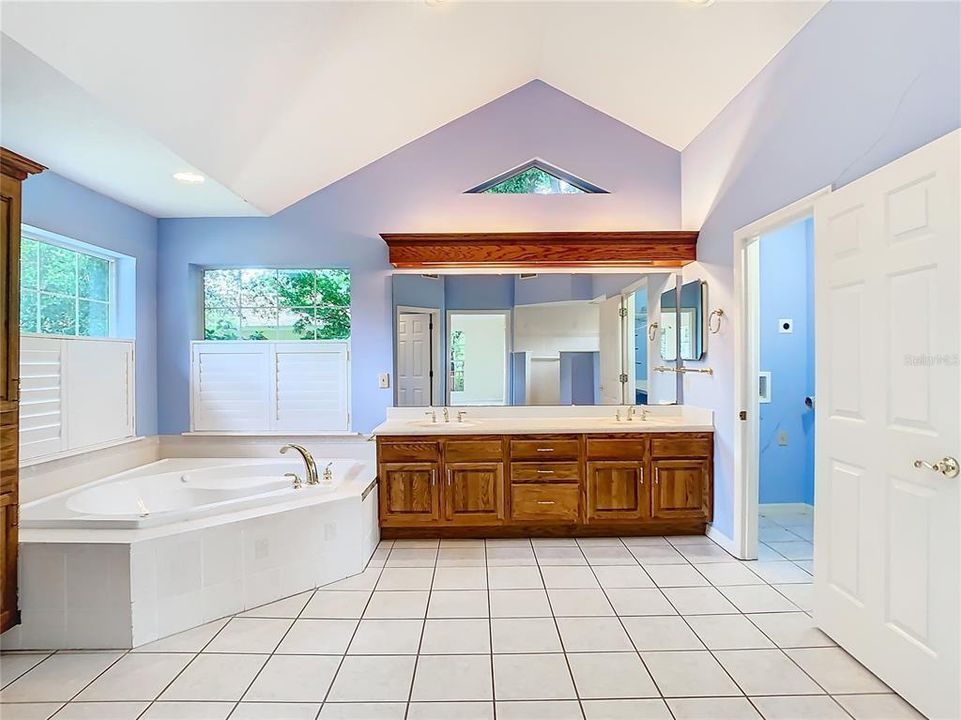 Mater bath with a dual sink vanity with ample storage space, garden tub with a lake view, separate water closet, and adjacent laundry room.