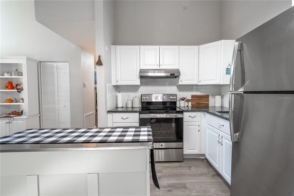 The kitchen features a high ceiling, vinyl flooring and neutral tones.