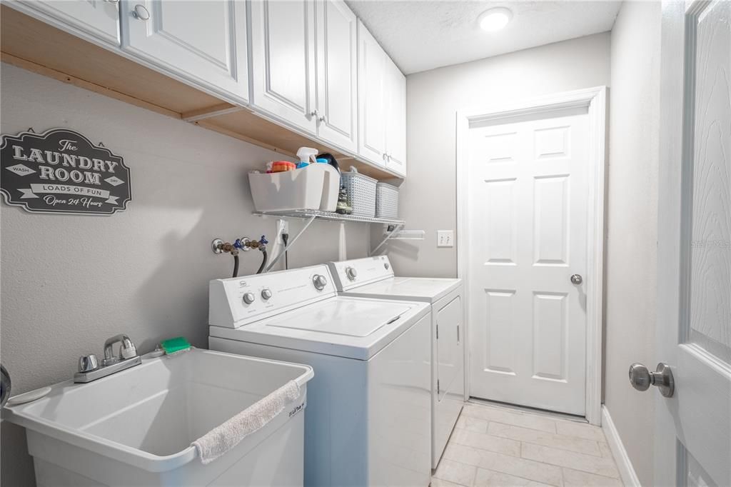 The laundry room is designed for efficiency and convenience, featuring durable tile flooring that stands up to daily use. Built-in overhead cabinetry offers ample storage for cleaning supplies and essentials, keeping everything neatly organized. The space includes a top-load washer and dryer, complemented by a handy shelf for additional storage. A utility sink adds practicality, perfect for tackling tough stains or cleaning tasks, making this laundry room a functional and well-equipped space.