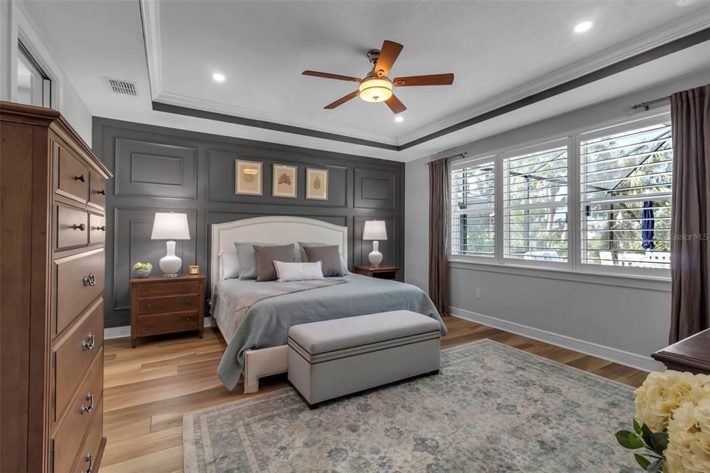 Primary bedroom with plantation shutters; designer wall and coffered ceiling