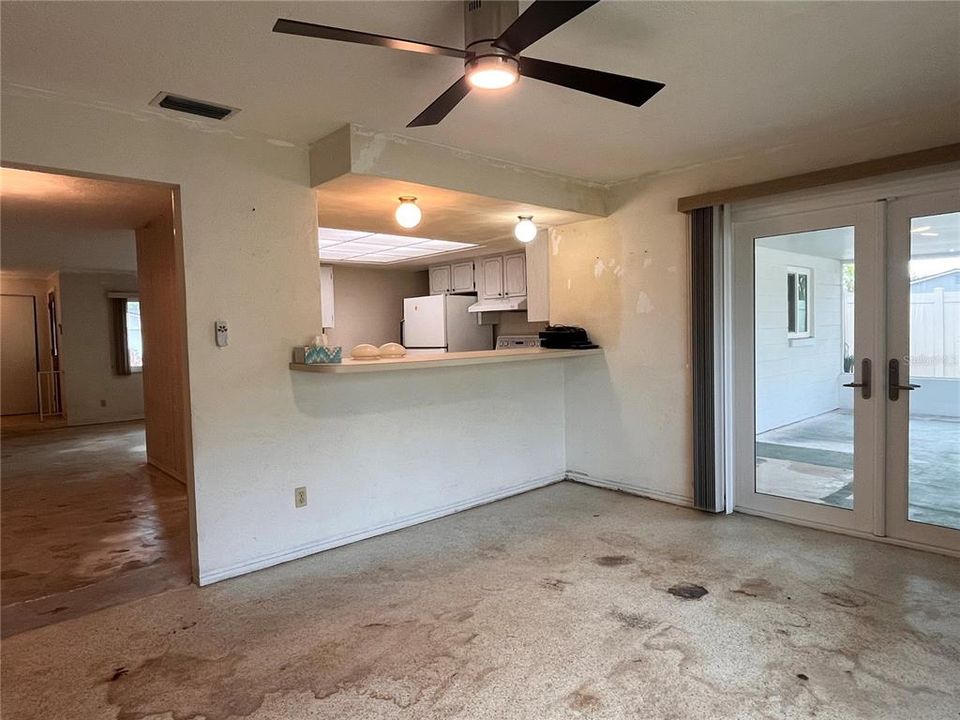 Family room with opening to kitchen.  Doors to screened porch with terrazzo floors (shows glue residue from carpet pulled up)